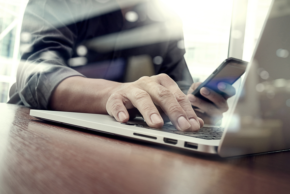 designer hand working and smart phone and laptop on wooden desk in office with london city background